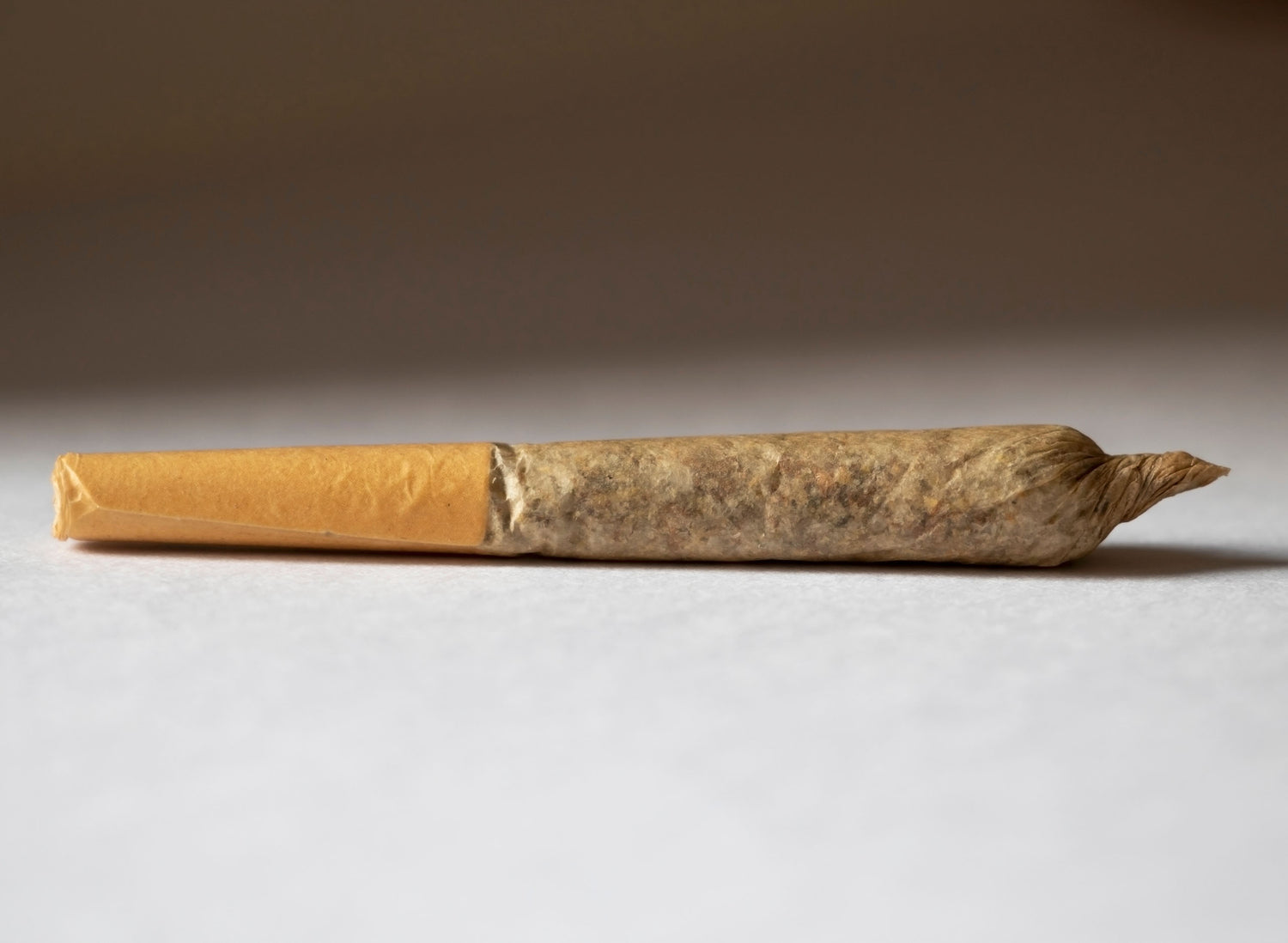 Blank white paper on orange envelope, surrounded by cigarettes, green leaves, a lemon, and small containers on black surface
