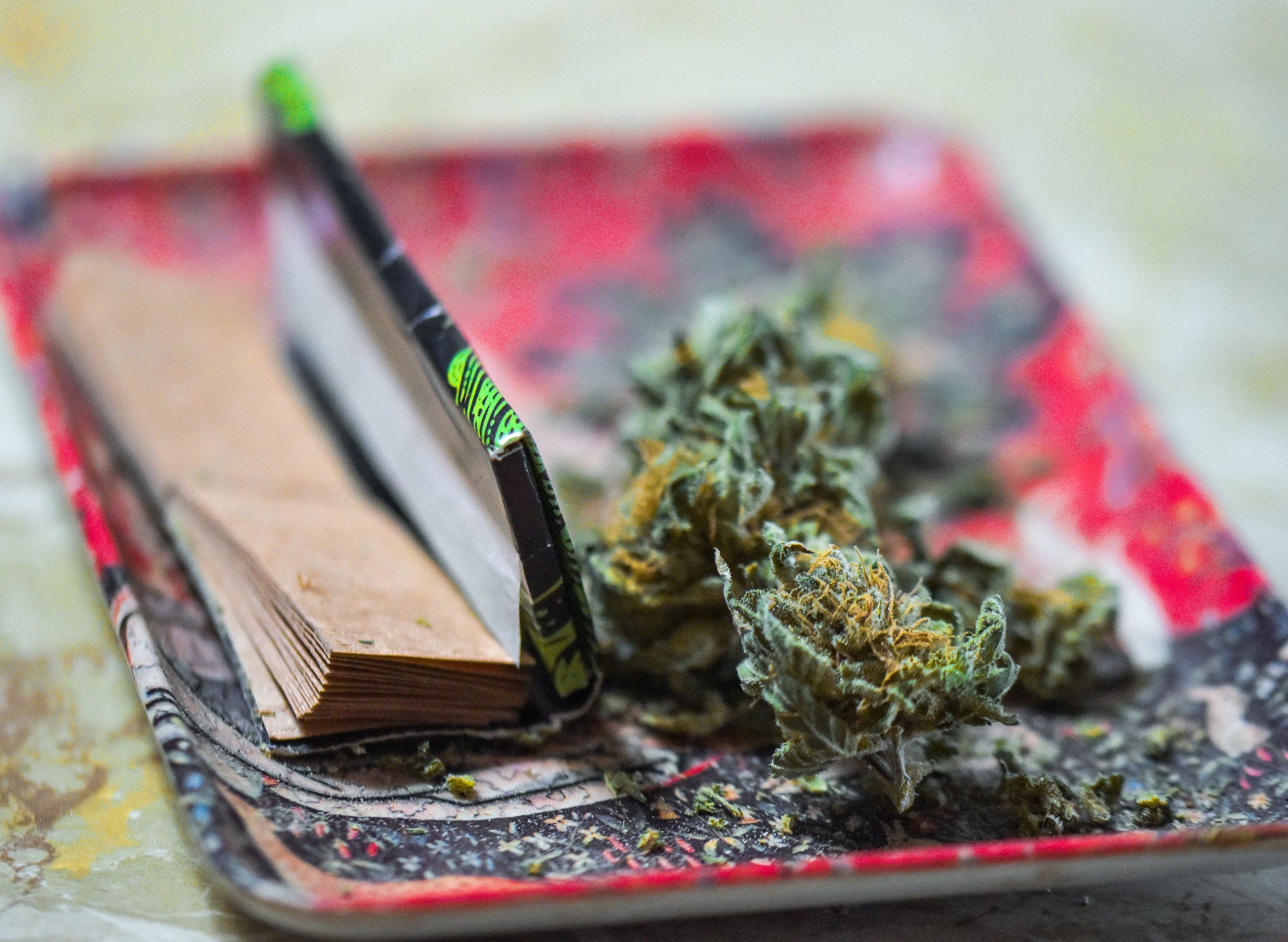 Glass bottles with droppers, cannabis leaves, and buds on books against a green background with soft lighting