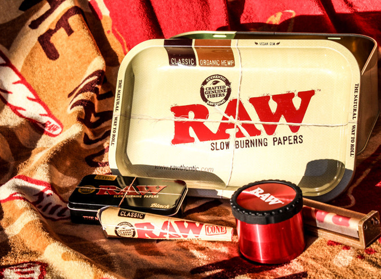 Brown box with "RAW" text, surrounded by cameras, film rolls, pens, bottles, and a straw hat on a black surface